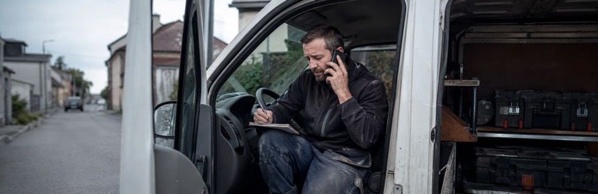 Handwerker sitzt im Transporter, telefoniert und macht sich Notizen